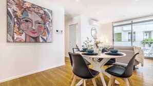 Un coin repas avec une table ronde, des chaises noires et un grand tableau abstrait accroché au mur.