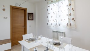 A dining area with a table set for four, a wooden door, a radiator, and a window with floral curtains. - Apartment 'Ca' Graziosi Cuori' with Mountain View, Shared Garden and Wi-Fi (Bagnone)