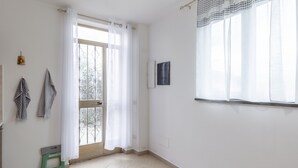 A room with a sliding glass door, a small green stool, a framed picture, and a window with sheer curtains. - Apartment 'Ca' Graziosi Cuori' with Mountain View, Shared Garden and Wi-Fi (Bagnone)