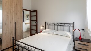 A bedroom with a bed, a nightstand, a red lamp, a wooden wardrobe, and a mirror. - Apartment 'Ca' Graziosi Fiori' with Mountain View, Shared Garden and Wi-Fi (Bagnone)
