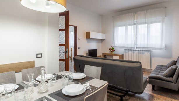 A dining area with a table set for four, a sofa, a TV, and a window with curtains. - Apartment 'Ca' Graziosi Fiori' with Mountain View, Shared Garden and Wi-Fi (Bagnone)