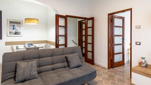 A living room with a sofa, a dining table with chairs, a pendant light, and a door with frosted glass panels. - Apartment 'Ca' Graziosi Fiori' with Mountain View, Shared Garden and Wi-Fi (Bagnone)