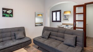 A modern living room with two grey sofas, a large mirror, and a dining area visible through an arched doorway. - Apartment 'Ca' Graziosi Fiori' with Mountain View, Shared Garden and Wi-Fi (Bagnone)