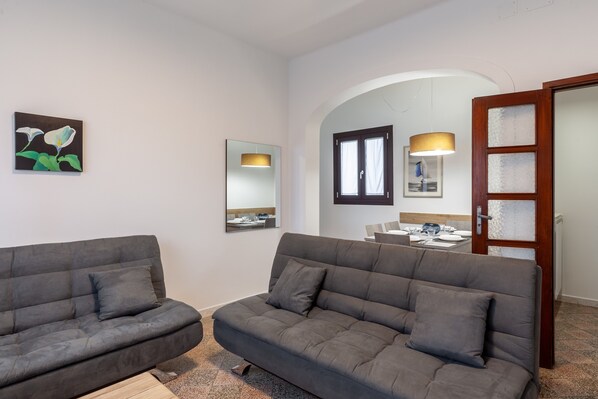 Una sala de estar moderna con dos sofás grises, un espejo grande y un comedor visible a través de un arco.