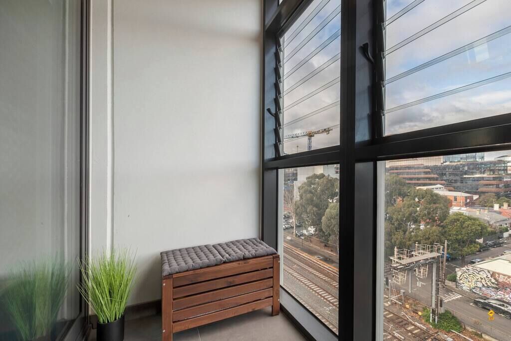Een balkon met een houten bankje, een plant in pot en uitzicht op de stadsgezicht door grote ramen.