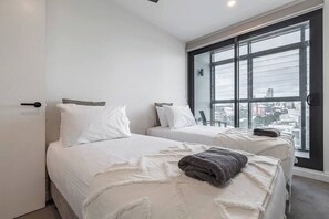 Quarto de hotel com duas camas, uma janela grande com vista para a cidade e uma porta com puxador.