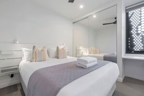 A modern bedroom with a large bed, a bedside table, a mirror, and a window with a geometric pattern.