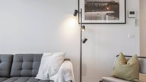 A modern living room with a grey sofa, a white pillow, a grey armchair, a floor lamp, and a framed picture on the wall.