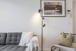 A modern living room with a grey sofa, a white pillow, a grey armchair, a floor lamp, and a framed picture on the wall.