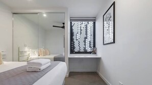 A modern hotel room with a large bed, a walk-in closet, a bathroom with a shower, and a window with a geometric pattern.
