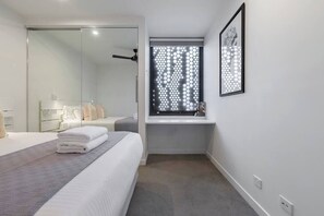 A modern hotel room with a large bed, a walk-in closet, a bathroom with a shower, and a window with a geometric pattern.
