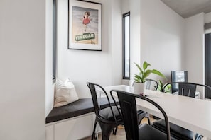 Uma cozinha moderna com bancada branca, cadeiras pretas, um vaso com planta e um cartaz emoldurado na parede.