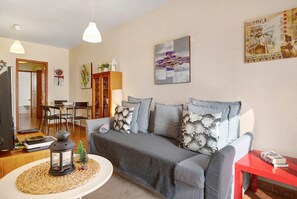 A living room with a grey sofa, a red side table, a small Christmas tree, and a wall-mounted artwork. - Vacation Home 'Luminoso Ático En Arrecife' with Private Terrace and Wi-Fi (Arrecife)