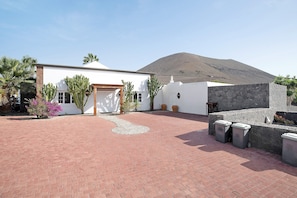 A house with a paved driveway, a stone wall, and a mountain in the background.
