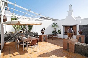 Une terrasse avec une table et des chaises, une pergola et un four en briques.