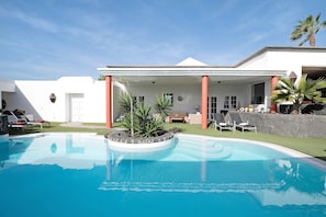 A swimming pool with a stone border, a covered patio area, and a white building with columns.