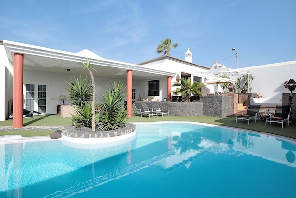 Une piscine avec, en arrière-plan, un bâtiment blanc, un mur de pierre et un palmier.