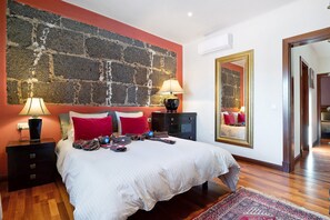 Une chambre avec un mur décoré d’un motif en briques, un grand lit avec une literie blanche, deux tables de chevet avec des lampes et un miroir au mur.