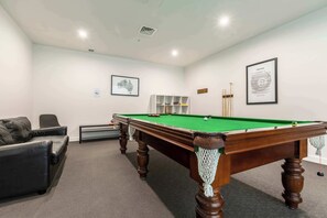 A billiards table in a room with a sofa, framed pictures, and a radiator.