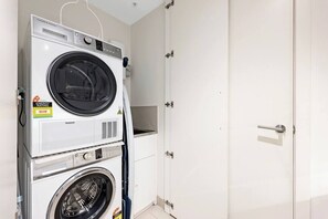 A laundry room with stacked washing machines and dryers, a white door, and a small shelf.