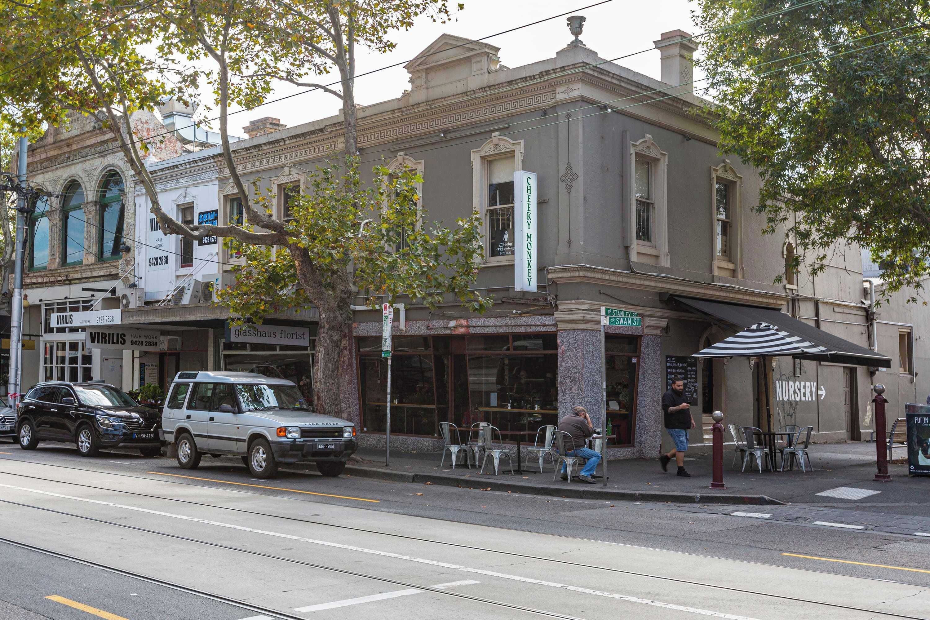 A street view with a building featuring a storefront, outdoor seating, and a sign for a nursery.