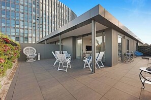 Ein modernes Gebäude mit einer überdachten Terrasse, ausgestattet mit weißen Stühlen und einem Tisch.