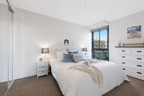 A bedroom with a large bed, bedside lamps, a nightstand, a dresser, and a window with a view.