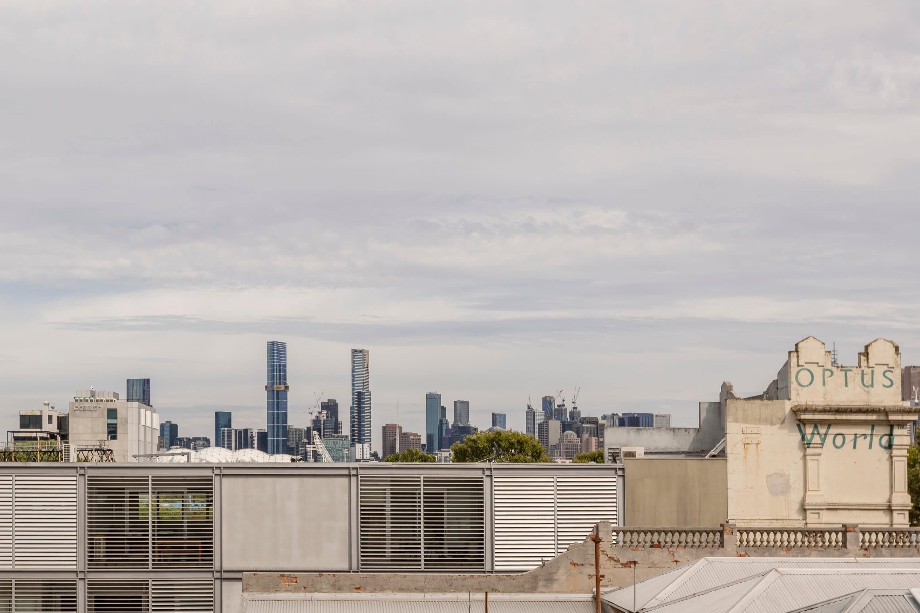 A city skyline with modern buildings, including a tall skyscraper, and a sign that reads 'Optus World'.