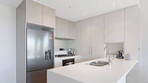 Una cocina moderna con un refrigerador de acero inoxidable, estufa a gas, pileta y muebles color blanco.