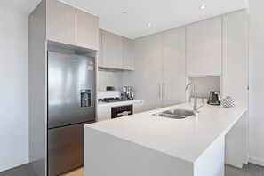 A modern kitchen with a stainless steel refrigerator, a gas stove, a sink, and white cabinetry.