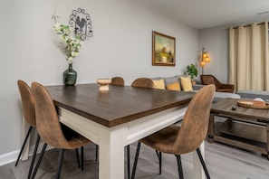 A dining area with a wooden table, brown upholstered chairs, a vase with flowers, a wall-mounted artwork, and a floor lamp. - Serene Oakwood Townhouse (Oakwood)