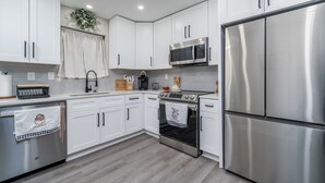 A modern kitchen with white cabinets, stainless steel appliances, and a wooden countertop.