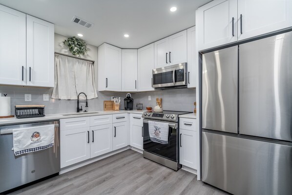 A modern kitchen with white cabinets, stainless steel appliances, and a wooden countertop.