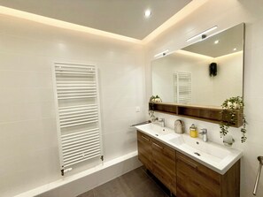 Features a towel rack, large mirror, and a vanity with a sink and shelf for toiletries.