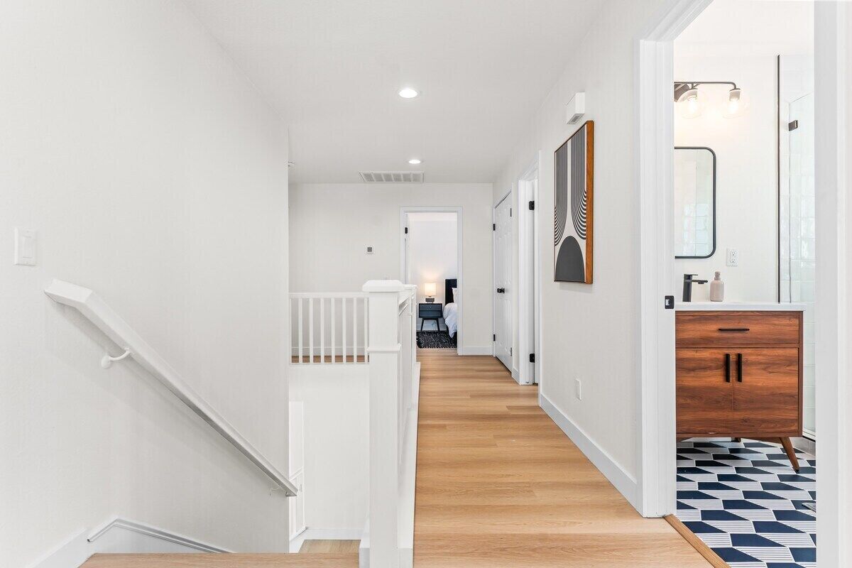A modern hallway with white walls, wooden flooring, and a staircase with white railings.