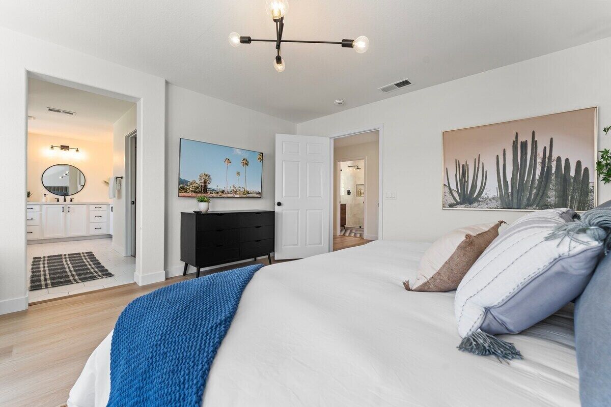 A bedroom with a bed, a dresser, a mirror, and a painting of cacti.