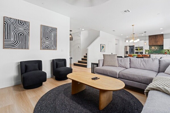 A modern living room with a sofa, two armchairs, a coffee table, and abstract wall art.