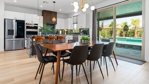 A modern kitchen with a dining area, large windows, and a view of a swimming pool. - Green Lion - New Spectacular Modern Pool home (Coachella)