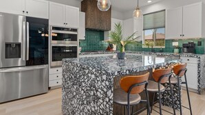 A modern kitchen with white cabinets, a granite island, stainless steel appliances, and pendant lighting. - Green Lion - New Spectacular Modern Pool home (Coachella)