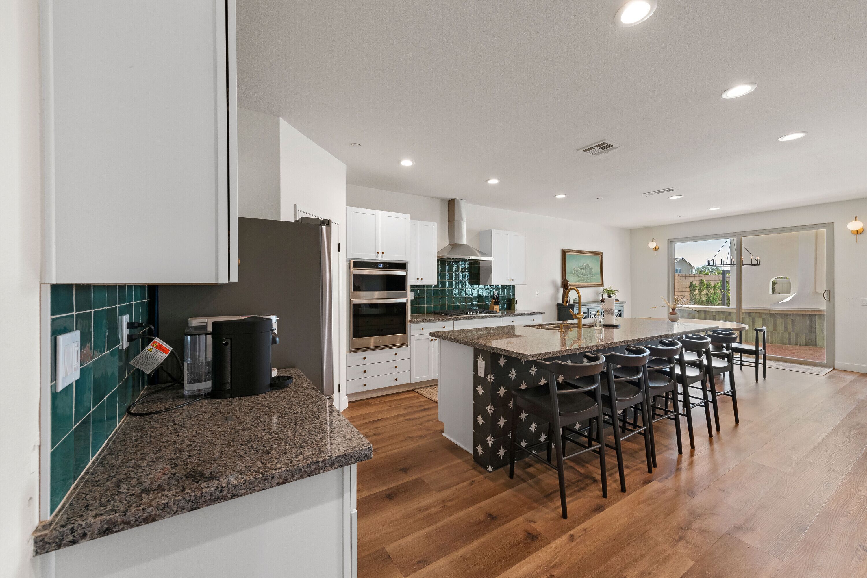 A modern kitchen with white cabinets, a central island with bar stools, and a view through the glass door.