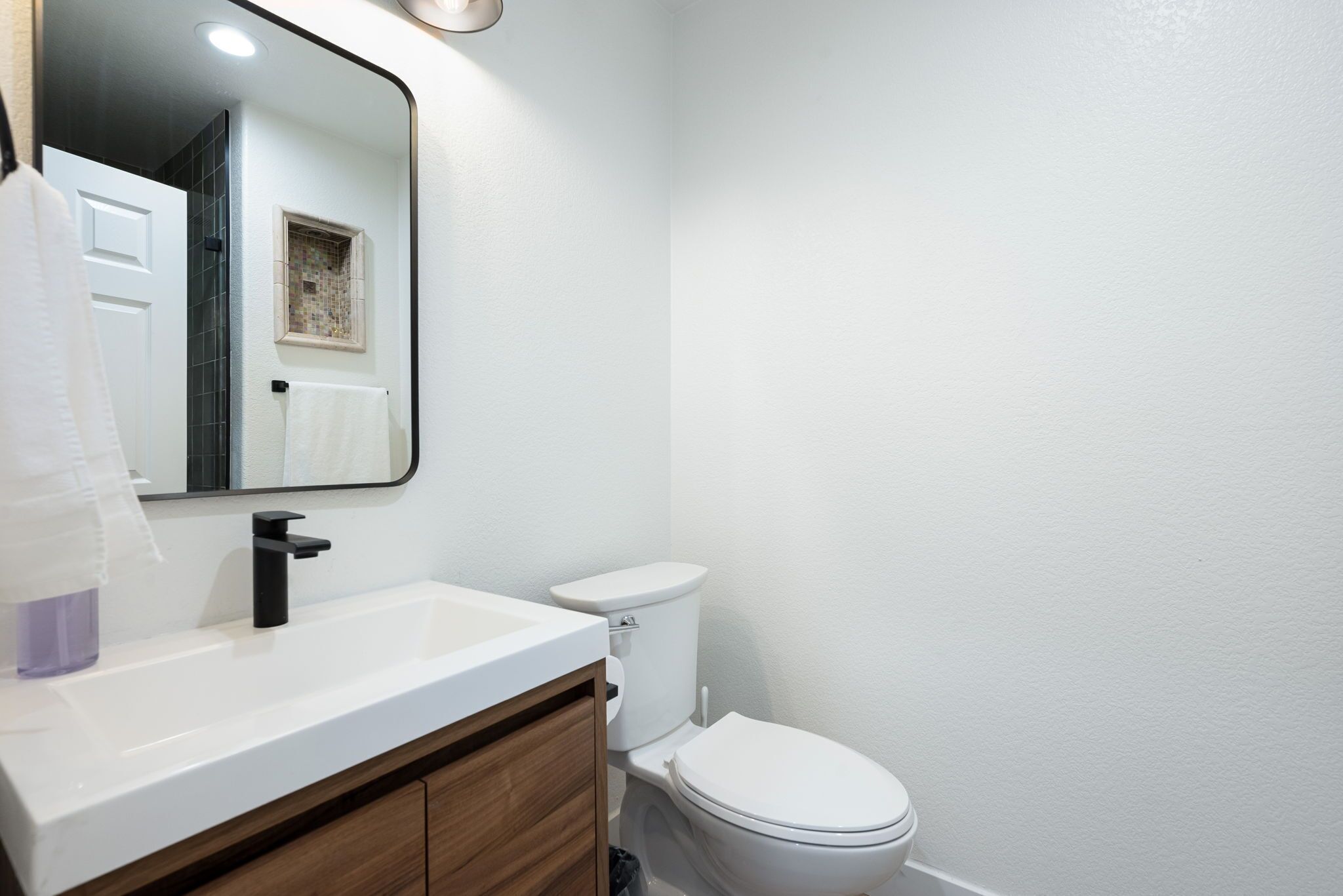 Une salle de bain avec un lavabo blanc, un robinet noir, des toilettes blanches et un miroir au-dessus du lavabo.