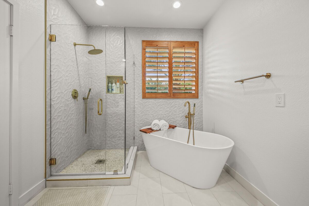 Ein modernes Badezimmer mit einer begehbaren Glasdusche, einer freistehenden Badewanne und einem Fenster mit Holzjalousien.