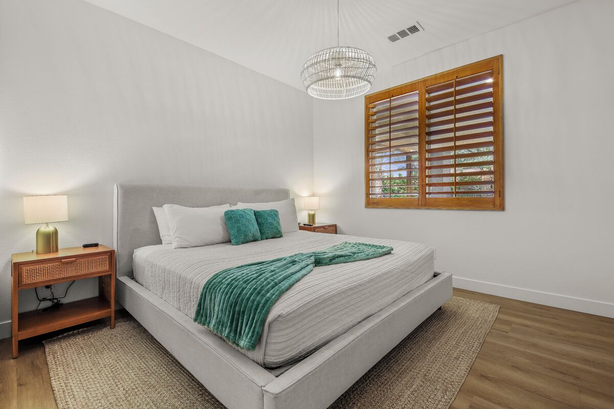 A bedroom with a bed, bedside lamps, a window with blinds, and a hanging light fixture.