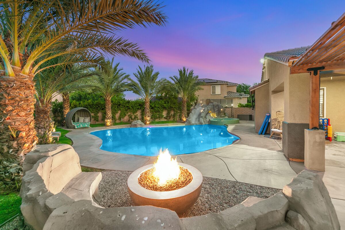 A backyard with a swimming pool, a fire pit, and palm trees.