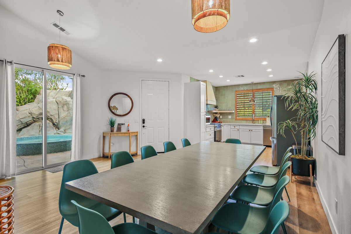 A modern kitchen with a large island, a dining area with a long table and chairs, and a view of a swimming pool through glass doors.