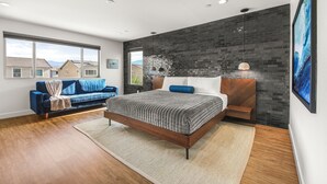 A modern bedroom with a large bed, a sofa, and a view of houses through a window. - Escape to this newly remodeled 7-bedroom desert retreat designed for relaxation and fun. Enjoy a large resort-style pool and spa, a fully stocked kitchen, spacious game room, and outdoor games perfect for group play under endless blue skies. Whether (Coachella)