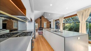 A modern kitchen with a central island, a brick wall, and a large window with curtains. - Waterfront Retreat - Kayaks, Heated Pool, Firepit and so much more!  (Lower Portland)
