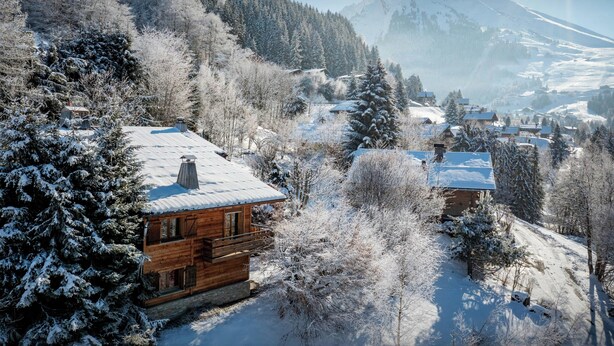 A wooden cabin with a snow-covered roof, surrounded by trees and a mountain in the background. - Chalet Paravis - La Clusaz stay for 9 sauna and games room - OVO Network (La Clusaz)