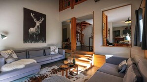 A modern living room with a grey sofa, a patterned throw, and a deer-themed pillow. A wooden staircase leads to an upper level. - Chalet Paravis - La Clusaz stay for 9 sauna and games room - OVO Network (La Clusaz)