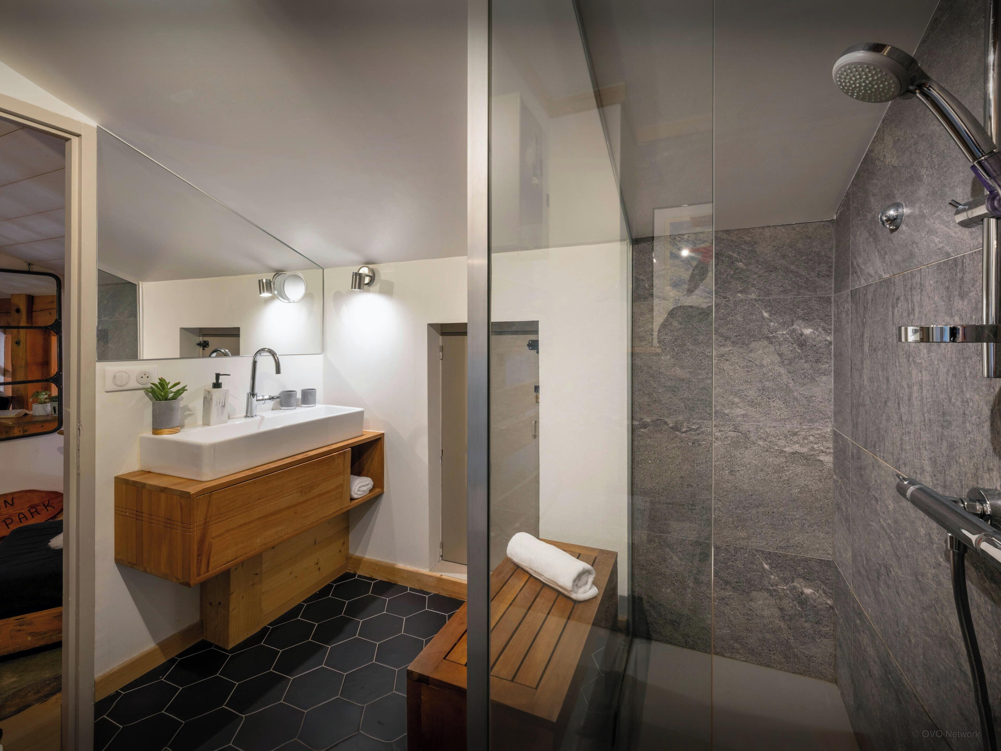 Een moderne badkamer met een glazen douchecabine, een houten wastafelmeubel en een vloer van zwart honingraatmozaïek.